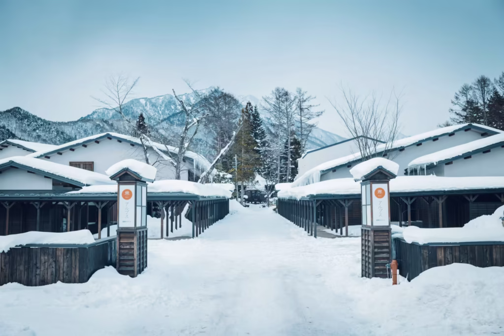 界 アルプスの冬景色。雪に包まれた和風の宿と、背景に広がる北アルプスの山並み